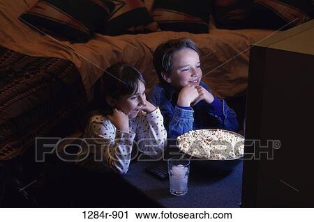 Boy and girl sitting in front of a bowl of popcorn watching television View Large Photo Image Stock Image - Boy and girl sitting in front of a bowl of popcorn watching television. Fotosearch