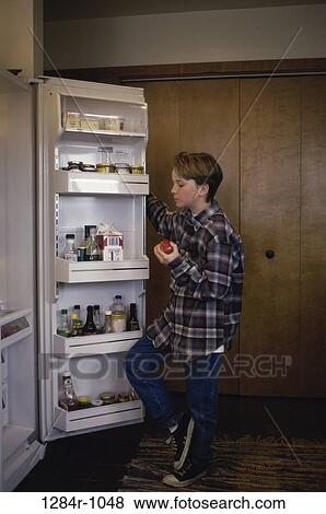 Stock Photo - Boy standing by a refrigerator holding an apple. Fotosearch