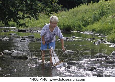 Boy standing in a creek with a toy sail boat View Large Photo Image Stock Photograph - Boy standing in a creek with a toy sail boat. Fotosearch
