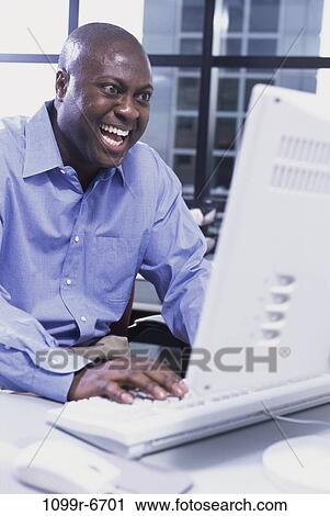 Businessman working on a computer laughing View Large Photo Image Stock Image - Businessman working on a computer laughing. Fotosearch