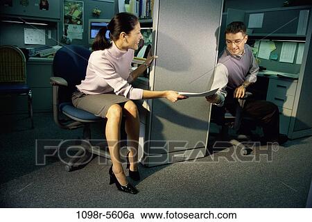 Stock Image - Businesswoman handing documents to a businessman in an office. Fotosearch