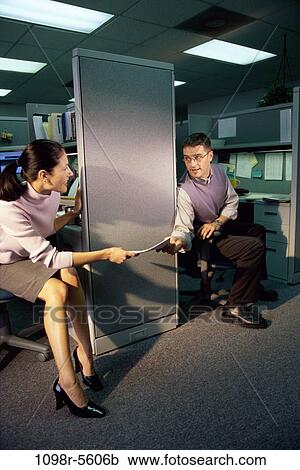 Stock Image - Businesswoman handing documents to a businessman in an office. Fotosearch