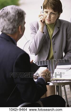 Businesswoman talking on a mobile phone sitting in front of a businessman View Large Photo Image Picture - Businesswoman talking on a mobile phone sitting in front of a businessman. Fotosearch