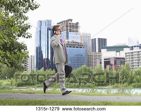 Canada, Alberta, Calgary, businessman talking on cell phone while walking along river path View Large Photo Image Stock Photo - Canada, Alberta, Calgary, businessman talking on cell phone while walking along river path. Fotosearch