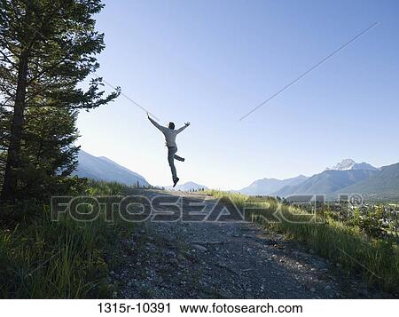 Stock Image - Canada, Alberta, Canmore, Rear view of man jumping above mountain trail. Fotosearch