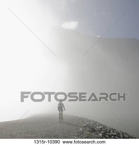 Canada, Alberta, Canmore, Silhouette of woman cycling down mountain road in fog View Large Photo Image Stock Image - Canada, Alberta, Canmore, Silhouette of woman cycling down mountain road in fog. Fotosearch