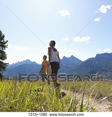 Stock Image - Canada, Alberta, couple walking along path through mountain meadow. Fotosearch