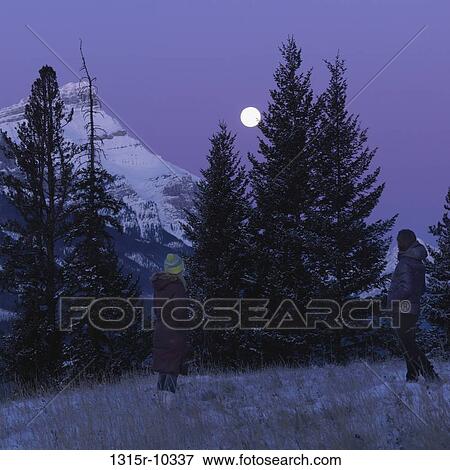 Canada, Alberta, couple watching moon from snowy mountain meadow View Large Photo Image Stock Photo - Canada, Alberta, couple watching moon from snowy mountain meadow. Fotosearch