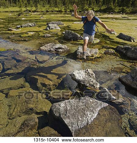 Canada, Alberta, Man jumping between boulders in mountain river View Large Photo Image Picture - Canada, Alberta, Man jumping between boulders in mountain river. Fotosearch