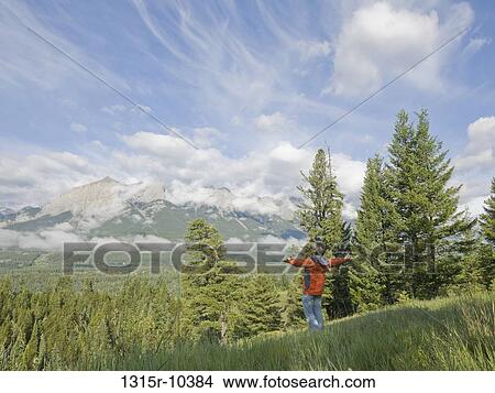 Picture - Canada, Alberta, Man standing in mountain meadow with arms outstretched. Fotosearch