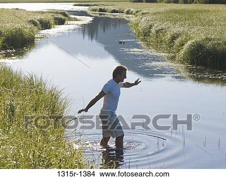 Picture - Canada, Alberta, man walking into creek from tall grasses. Fotosearch