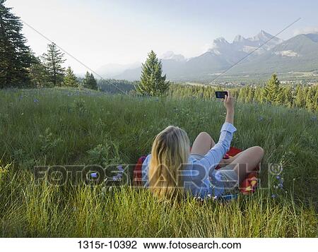Stock Image - Canada, Alberta, Rear view of woman photographing landscape on mountain meadow. Fotosearch