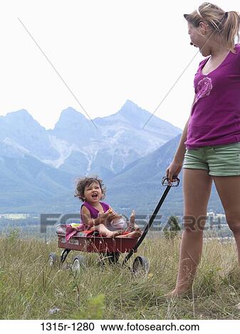 Canada, Alberta, teenage girl pulling baby girl in red wagon with mountains in background View Large Photo Image Stock Image - Canada, Alberta, teenage girl pulling baby girl in red wagon with mountains in background. Fotosearch