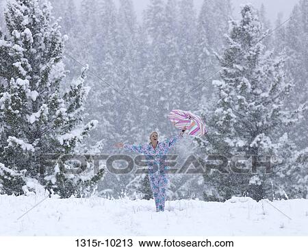 Stock Image - Canada, Alberta, Woman standing in snow and holding umbrella overhead. Fotosearch