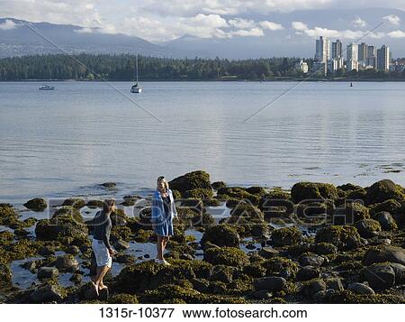 Canada, British Columbia, Vancouver, Couple walking through algae covered tidal rocks, downtown skyline in background View Large Photo Image Stock Photo - Canada, British Columbia, Vancouver, Couple walking through algae covered tidal rocks, downtown skyline in background. Fotosearch