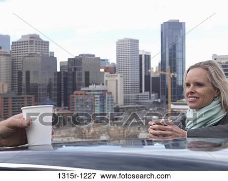 Stock Photo - Canada, Calgary, Two business people drinking coffees on roof above downtown skyline. Fotosearch