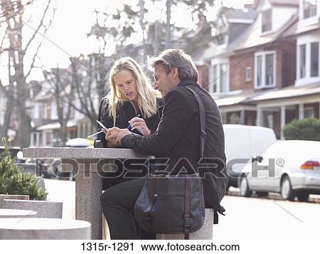 Canada, Ontario, Toronto, business couple checking text message on outdoor table View Large Photo Image Stock Image - Canada, Ontario, Toronto, business couple checking text message on outdoor table. Fotosearch