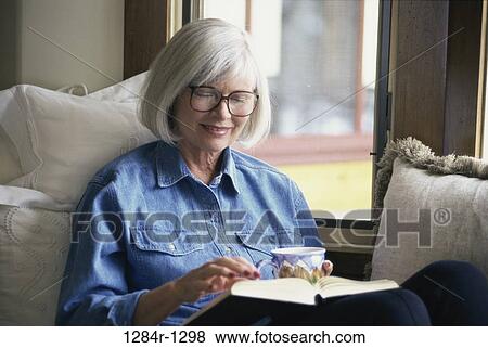 Close-up of a senior woman sitting on a couch reading a book View Large Photo Image Stock Photo - Close-up of a senior woman sitting on a couch reading a book. Fotosearch