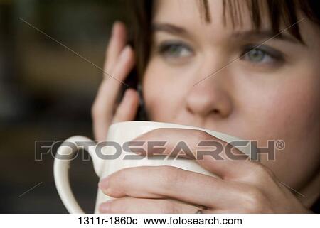 Stock Image - Close-up of a young woman drinking coffee and using a mobile phone. Fotosearch
