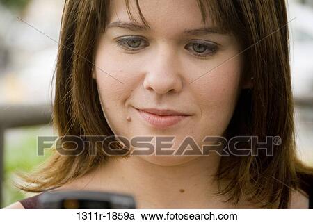 Stock Image - Close-up of a young woman reading text messaging on a mobile phone. Fotosearch
