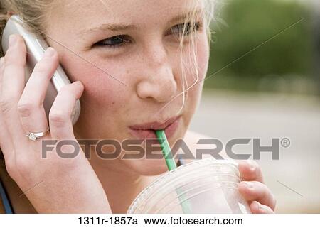 Stock Image - Close-up of a young woman talking on a mobile phone and sipping cold drink. Fotosearch