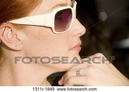 Close-up of a young woman wearing sunglasses with her hand on her chin View Large Photo Image Stock Photo - Close-up of a young woman wearing sunglasses with her hand on her chin. Fotosearch