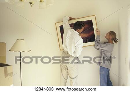 Stock Image - Couple hanging a picture frame on the wall. Fotosearch
