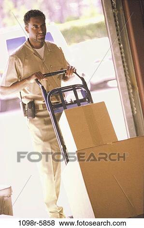Stock Photo - Delivery man pushing boxes in a warehouse. Fotosearch