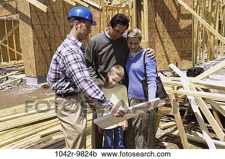 Stock Image - Family standing at a construction site with a worker holding blueprints. Fotosearch