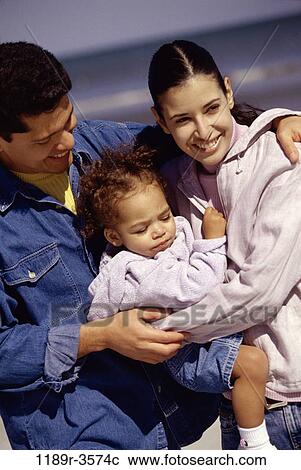 Stock Image - Father and mother on the beach holding their daughter. Fotosearch