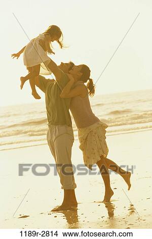Picture - Father and mother playing with their daughter on the beach. Fotosearch