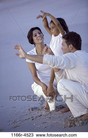Stock Image - Father and mother playing with their daughter on the beach. Fotosearch