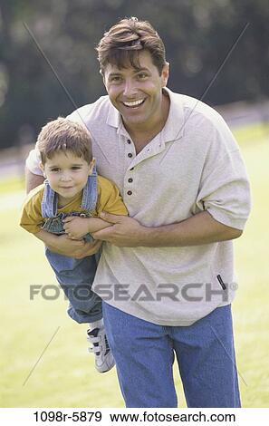 Father carrying his son in a park View Large Photo Image Stock Photo - Father carrying his son in a park. Fotosearch