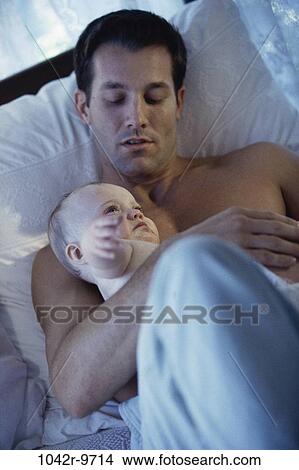Picture - Father lying with his baby boy on a bed. Fotosearch