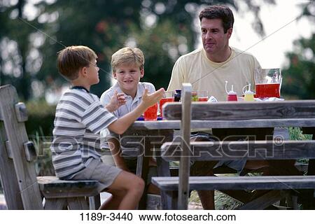 Father with his two sons seated on a picnic table View Large Photo Image Stock Image - Father with his two sons seated on a picnic table. Fotosearch