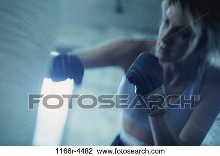 Stock Image - Female boxer punching a punching bag. Fotosearch