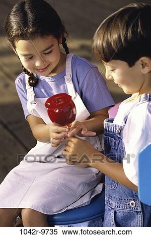 Girl and a boy sitting together holding a candy apple View Large Photo Image Stock Photography - Girl and a boy sitting together holding a candy apple. Fotosearch