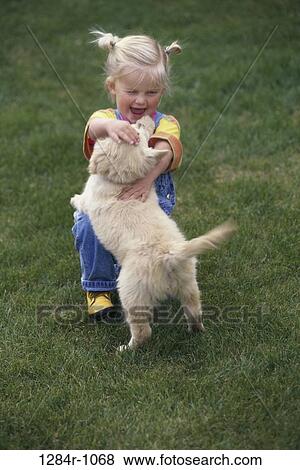 Stock Photo - Girl playing with a puppy on a lawn. Fotosearch