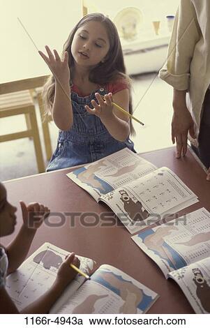 Stock Image - Girl seated at a table counting on her fingers. Fotosearch