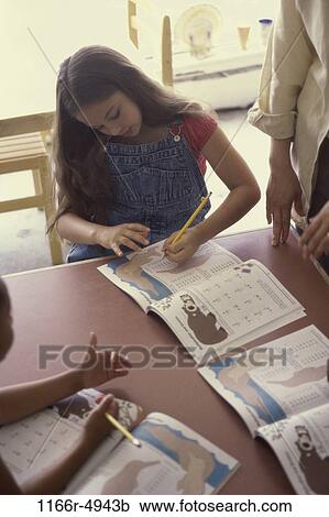 Stock Image - Girl seated at a table writing in a book. Fotosearch