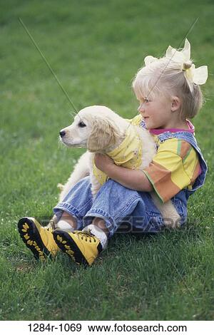 Girl sitting on a lawn holding a puppy View Large Photo Image Stock Photo - Girl sitting on a lawn holding a puppy. Fotosearch