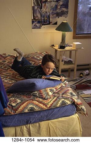 Picture - High angle view of a boy lying in bed reading. Fotosearch