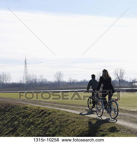 Italy, Couple bike along raised dike above field, power pylons View Large Photo Image Stock Photo - Italy, Couple bike along raised dike above field, power pylons. Fotosearch