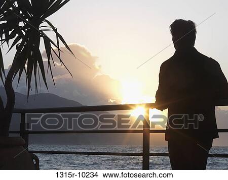 Picture - Italy, Liguria, Cinque Terre, Monterosso al Mare, Man looking at sun setting above sea. Fotosearch