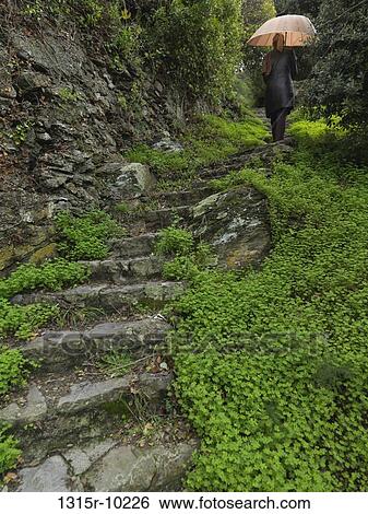 Stock Photograph - Italy, Liguria, Cinque Terre, Monterosso al Mare, Woman walking up path with umbrella. Fotosearch