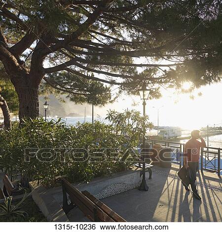 Italy, Liguria, Cinque Terre, Monterosso al Mare, Man walking along waterfront and talking on cell phone View Large Photo Image Stock Photograph - Italy, Liguria, Cinque Terre, Monterosso al Mare, Man walking along waterfront and talking on cell phone. Fotosearch