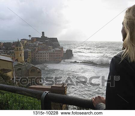 Stock Photo - Italy, Liguria, Cinque Terre, Vernazza, Woman watching surf crashing against breakwater. Fotosearch