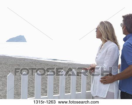 Italy, Liguria, Couple looking out across beach to distant island from picket fence View Large Photo Image Stock Image - Italy, Liguria, Couple looking out across beach to distant island from picket fence. Fotosearch