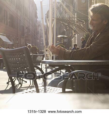 Stock Photo - Italy, Liguria, Man sending text message from outdoor cafe. Fotosearch