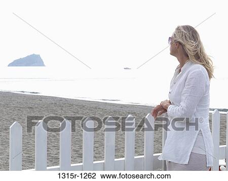 Italy, Liguria, Woman looking out across beach from picket fence View Large Photo Image Stock Image - Italy, Liguria, Woman looking out across beach from picket fence. Fotosearch